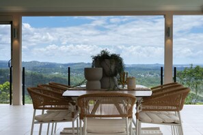 A dining area with a table and chairs, a large potted plant, and a view of a mountainous landscape. - Luxury 6BR Hinterland Retreat w/ Pool &Scenic View (Bonogin)