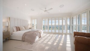 Ein Schlafzimmer mit einem Bett, einem Nachttisch, einem Deckenventilator und großen Fenstern.