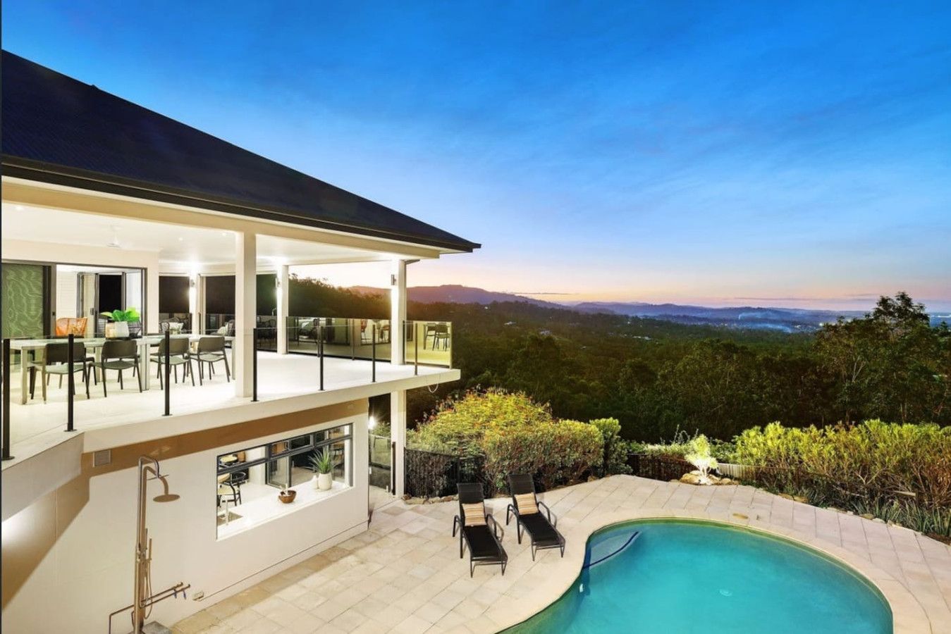 A modern two-story house with a swimming pool, outdoor seating, and a view of the surrounding landscape.