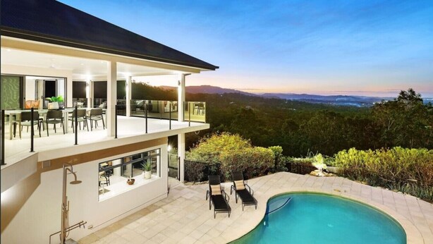 Ein modernes, zweistöckiges Haus mit Swimmingpool, Sitzgelegenheiten im Freien und Blick auf die umliegende Landschaft.