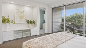 Un dormitorio con una cama, un banco, dos plantas en macetas, una obra de arte enmarcada y un ventanal corredero que da a un espacio exterior.