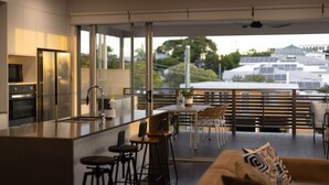 Cocina moderna con una isla grande, taburetes de bar y un comedor con vistas a paneles solares y vegetación.
