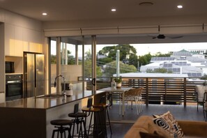 A modern kitchen with a large island, bar stools, and a dining area with a view of solar panels and greenery.