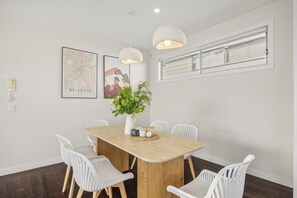 A dining area with a wooden table, white chairs, a vase with flowers, and two pendant lights.