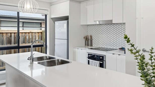 A modern kitchen with white cabinetry, a stainless steel sink, a built-in dishwasher, and a window with a view of a wooden deck. - Newly Furnished Stylish 4BR Getaway with Patio (Park Ridge)