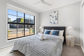 A bedroom with a large window, a bed with a grey blanket, two bedside lamps, and a ceiling fan.
