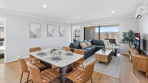 A modern living room with a dining area, a sofa set, and a TV. - Newly Furnished Stylish 4BR Getaway with Patio (Park Ridge)