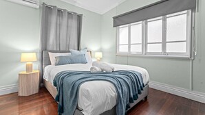 Ein Schlafzimmer mit einem Bett, zwei Nachttischlampen, einem Fenster mit Jalousie und einem Vorhang.