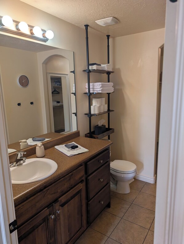 A bathroom with a vanity, sink, mirror, and shelves with towels.