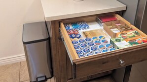 A kitchen with a coffee maker, a trash bin, and a drawer with food items.