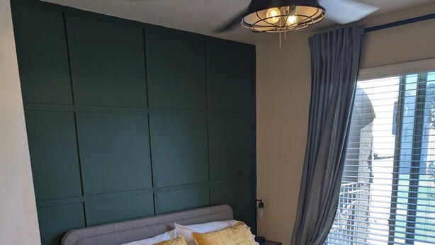 A neatly made bed with a patterned bedspread, a ceiling fan, and a window with curtains.