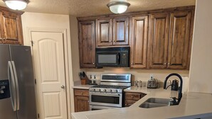 A kitchen with wooden cabinets, a stainless steel refrigerator, a microwave, an oven, and a sink.