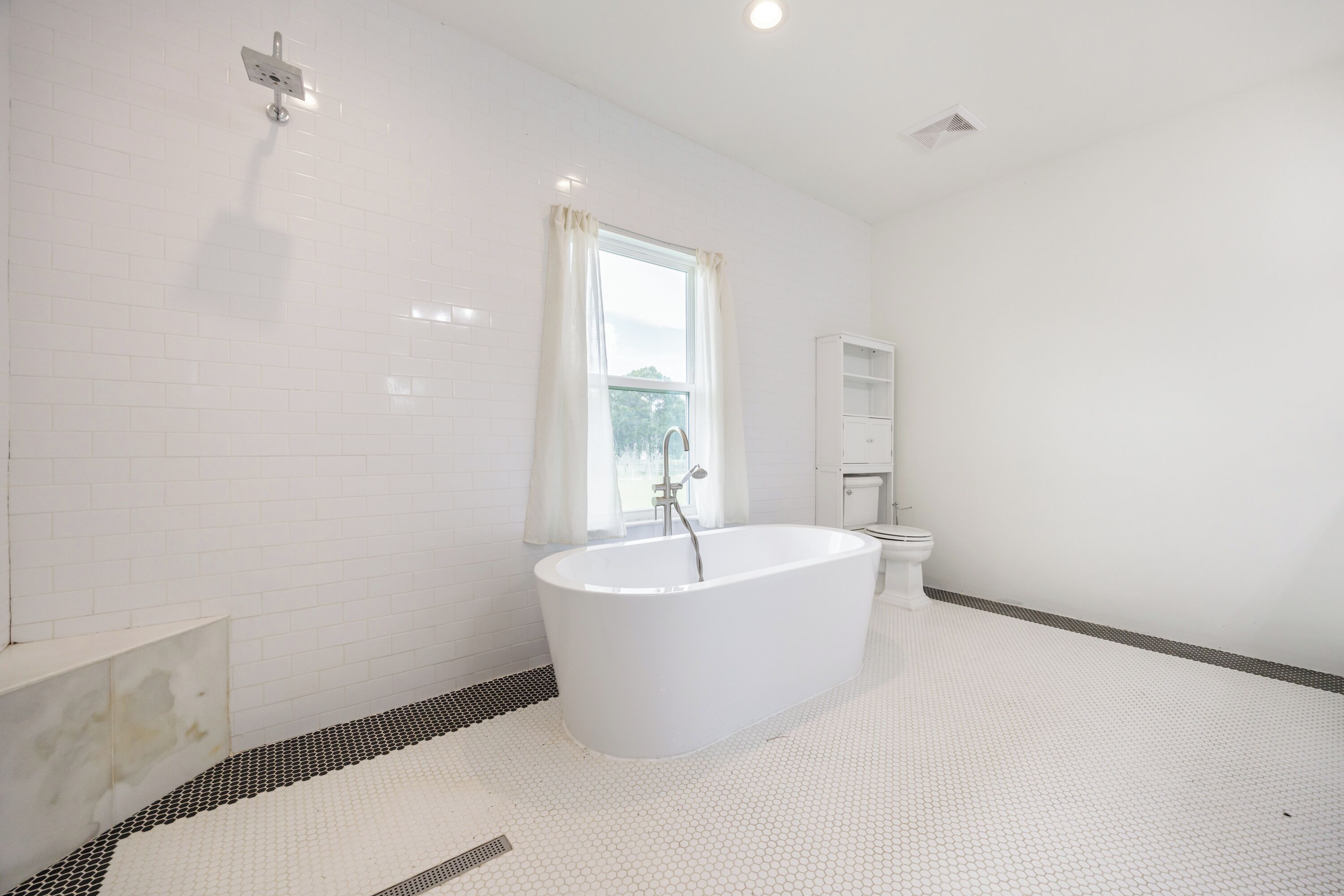 A modern bathroom with a freestanding bathtub, a toilet, and a window with curtains.