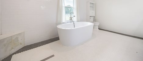 A modern bathroom with a freestanding bathtub, a toilet, and a window with curtains.