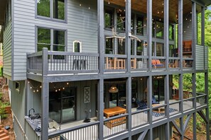 A multi-level wooden house with balconies, outdoor seating, and string lights. - Moonlight Creek Retreat ~ Private Creek, Hot Tub, Fire Pit & More (Ellijay)