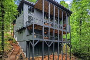 A multi-story wooden house with a balcony on the upper floor, surrounded by trees. - Moonlight Creek Retreat ~ Private Creek, Hot Tub, Fire Pit & More (Ellijay)