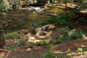 A stone fire pit surrounded by outdoor seating, a small stream, and string lights. - Moonlight Creek Retreat ~ Private Creek, Hot Tub, Fire Pit & More (Ellijay)