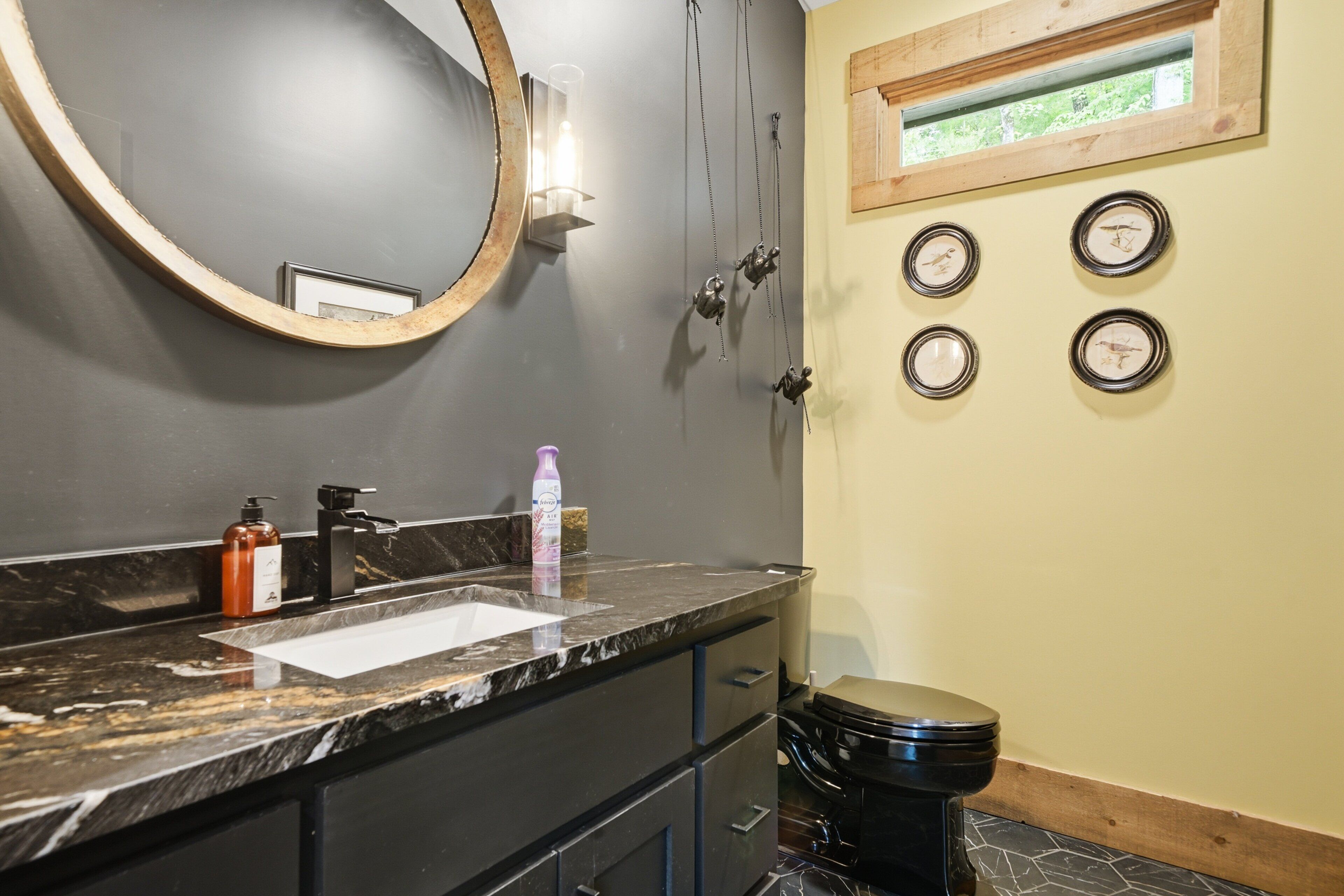 A bathroom with a marble sink, a round mirror, a toilet, and a wall clock.