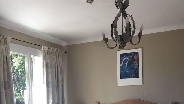 Une chambre à coucher avec un lit, des rideaux, un lustre, une table de chevet, une lampe et un tableau au mur.
