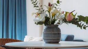 Une table de salle à manger ronde, entourée de chaises en osier, un vase rempli de fleurs, un rideau bleu et un tableau encadré accroché au mur.