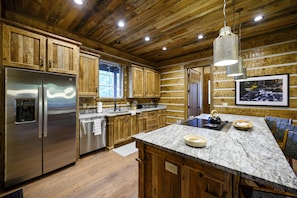 A kitchen with wooden cabinets, stainless steel appliances, a marble countertop, and a hanging light fixture. - Father & Son Built Cabin • Escape Room + Laser Tag • Sleeps 15 (Broken Bow)