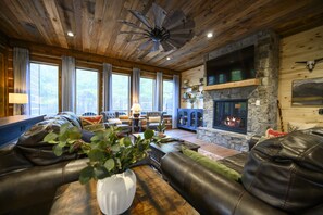 A cozy living room with leather sofas, a stone fireplace, and a wooden ceiling fan. - Father & Son Built Cabin • Escape Room + Laser Tag • Sleeps 15 (Broken Bow)