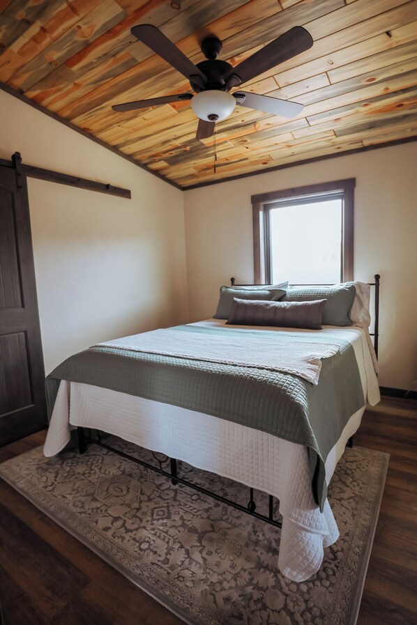 Une chambre à coucher avec un lit, un ventilateur de plafond, une fenêtre et une porte.