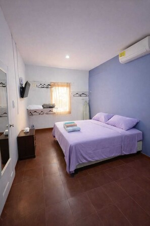 Ein Schlafzimmer mit einem Bett, einem kleinen Nachttisch, einem Spiegel, einem an der Wand montierten Fernseher und einem Fenster mit Vorhängen.