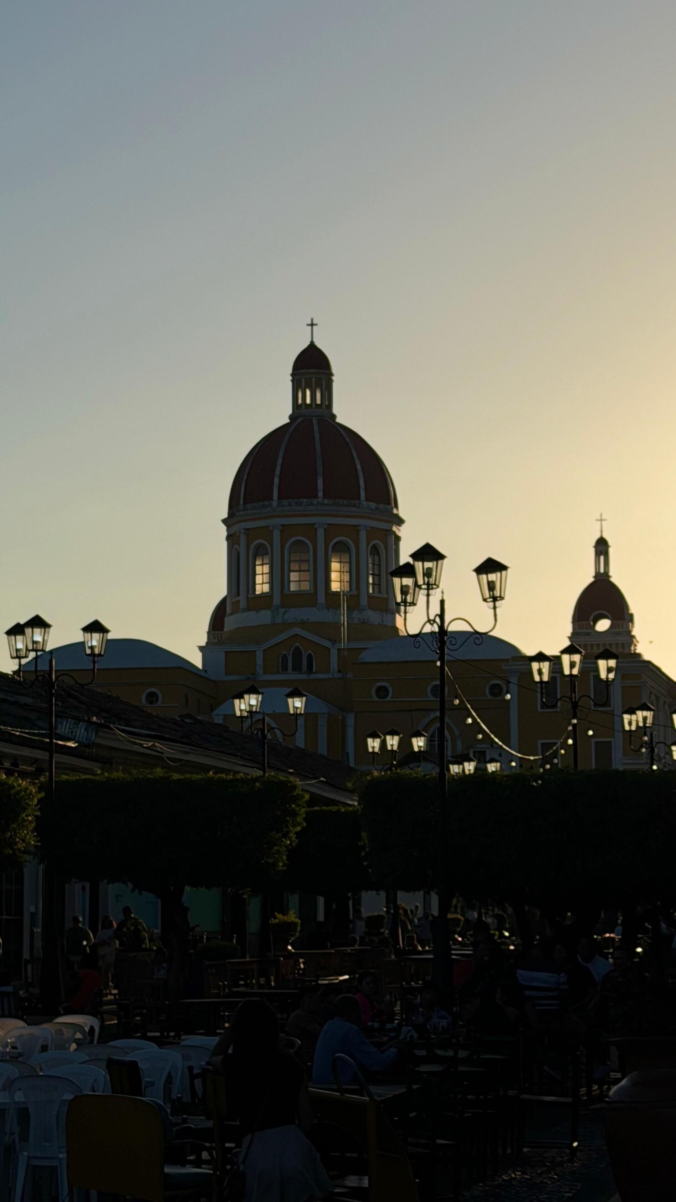 A building with a prominent dome and a cross on top, surrounded by outdoor seating areas.