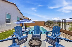 Un jardin avec une piscine, deux fauteuils Adirondack, un foyer extérieur et un parasol à rayures.