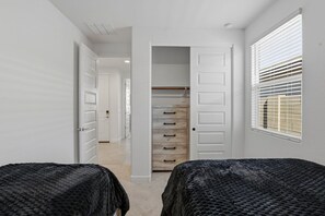 Une chambre avec deux lits, une armoire avec de nombreux tiroirs et une fenêtre avec des stores.