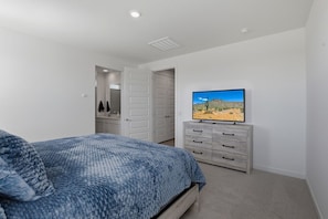 A bedroom with a bed, a television on a dresser, and a door leading to another room. - Blue Desert Oasis - 4 Bed w/ Bonus Casita and Pool and Firepit (Goodyear)