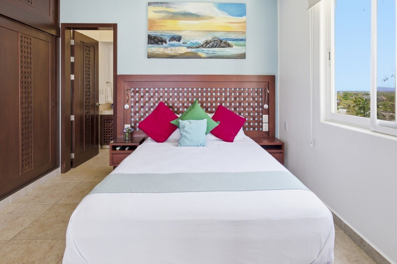 A hotel room with a bed, a headboard, a painting, and a window with a view.