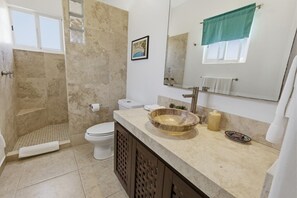 A bathroom with a stone sink, toilet, shower, and a large mirror. - 445 - Two Bedroom Ocean View (Bajos de Chila)
