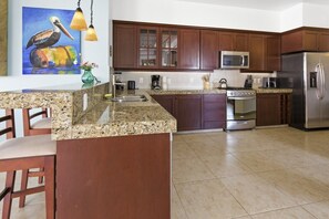 A kitchen with granite countertops, wooden cabinets, stainless steel appliances, and a painting of a pelican.