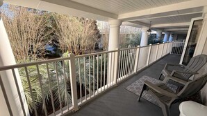 A covered outdoor area with a railing, chairs, and a view of trees and plants. - 1BR/1BA in Baytowne Wharf's Grand Sandestin (Miramar Beach)