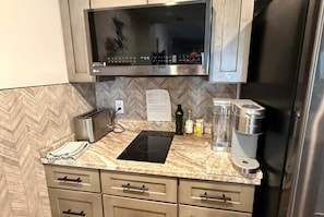 Una cocina con microondas, tostadora, cafetera y un salpicadero con estampado de espiga.