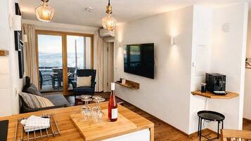 A modern living room with a large window, a flat-screen TV, and a wooden dining table.