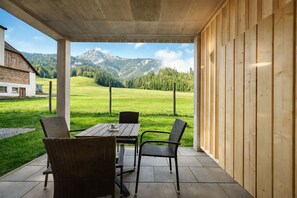 Eine überdachte Terrasse mit Tisch und Stühlen, mit Blick auf ein grünes Feld und Berge.