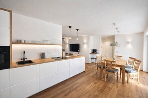 A modern kitchen with a wooden countertop, white cabinets, and a dining area with wooden chairs and a table.