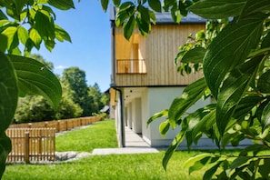 A two-story building with a balcony, surrounded by a wooden fence and greenery.