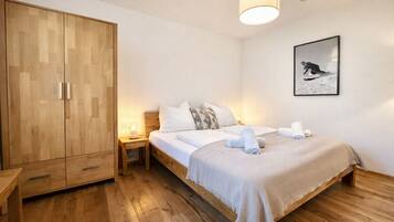 A bedroom with a wooden wardrobe, a bed with white bedding, a bedside table with a lamp, and a framed picture on the wall.