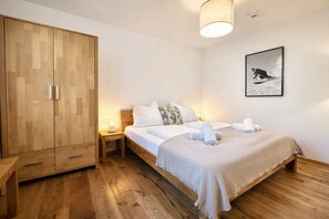 Un dormitorio con un armario de madera, una cama con ropa de cama blanca, una mesita de noche con lámpara y un cuadro en la pared.