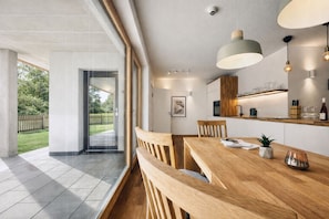 Eine moderne Küche mit Holdekor, ein Essbereich mit einem Holztisch und Bänken sowie ein Blick auf einen Garten durch eine Glastür.