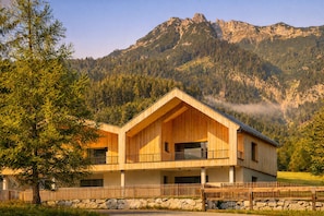 A wooden chalet with a balcony, set against a mountainous backdrop.