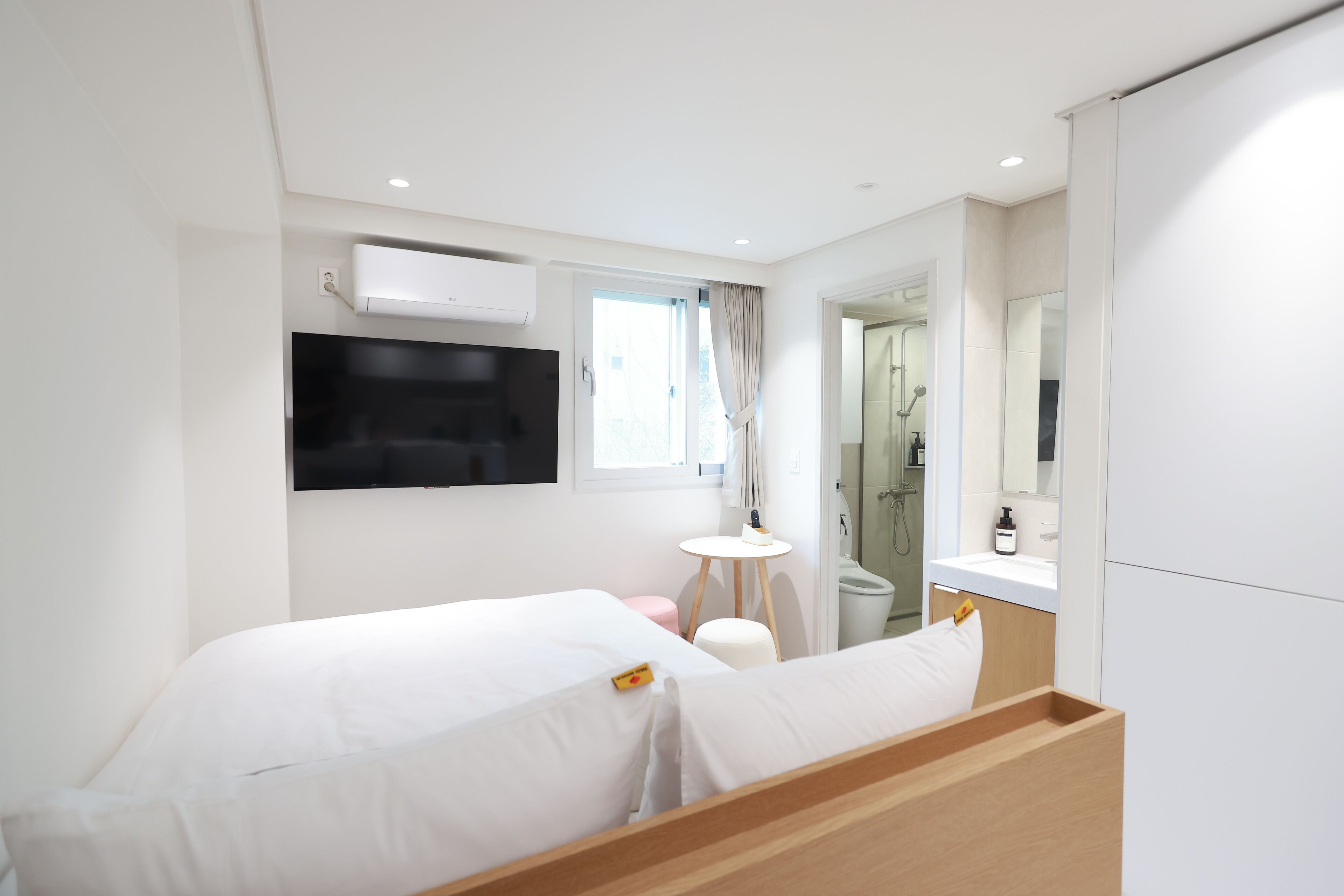 A modern hotel room with a bed, a small round table, a mirror, and a shower area.