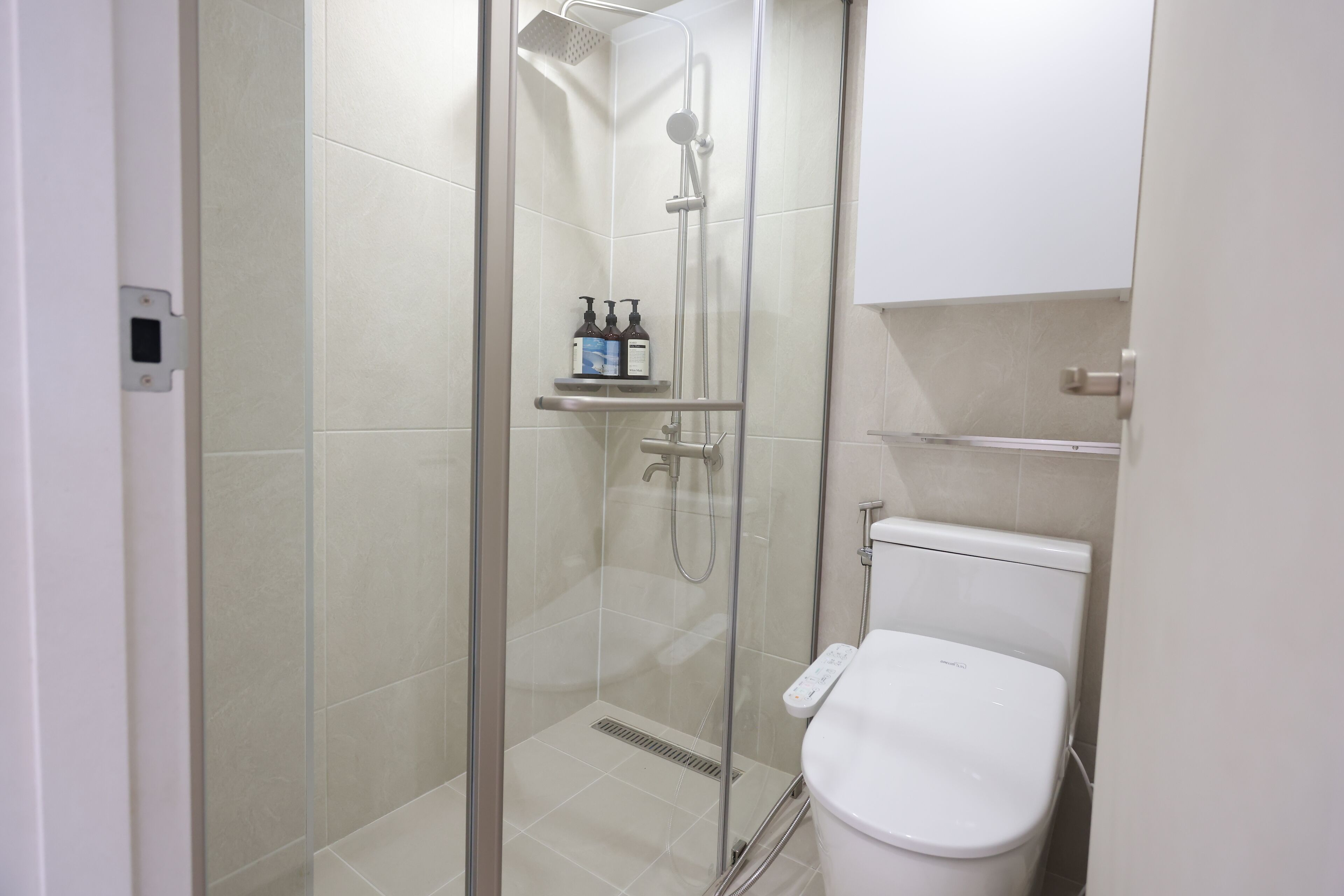 A modern bathroom with a glass-enclosed shower, a white toilet, and a shelf with toiletries.