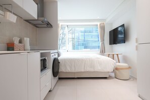 A modern hotel room with a bed, a washing machine, a small table, and a TV mounted on the wall. - Sinchon Stay (Seoul)
