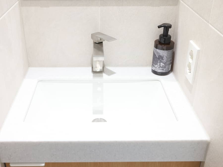 A bathroom with a white sink, a soap dispenser, and a towel rack.