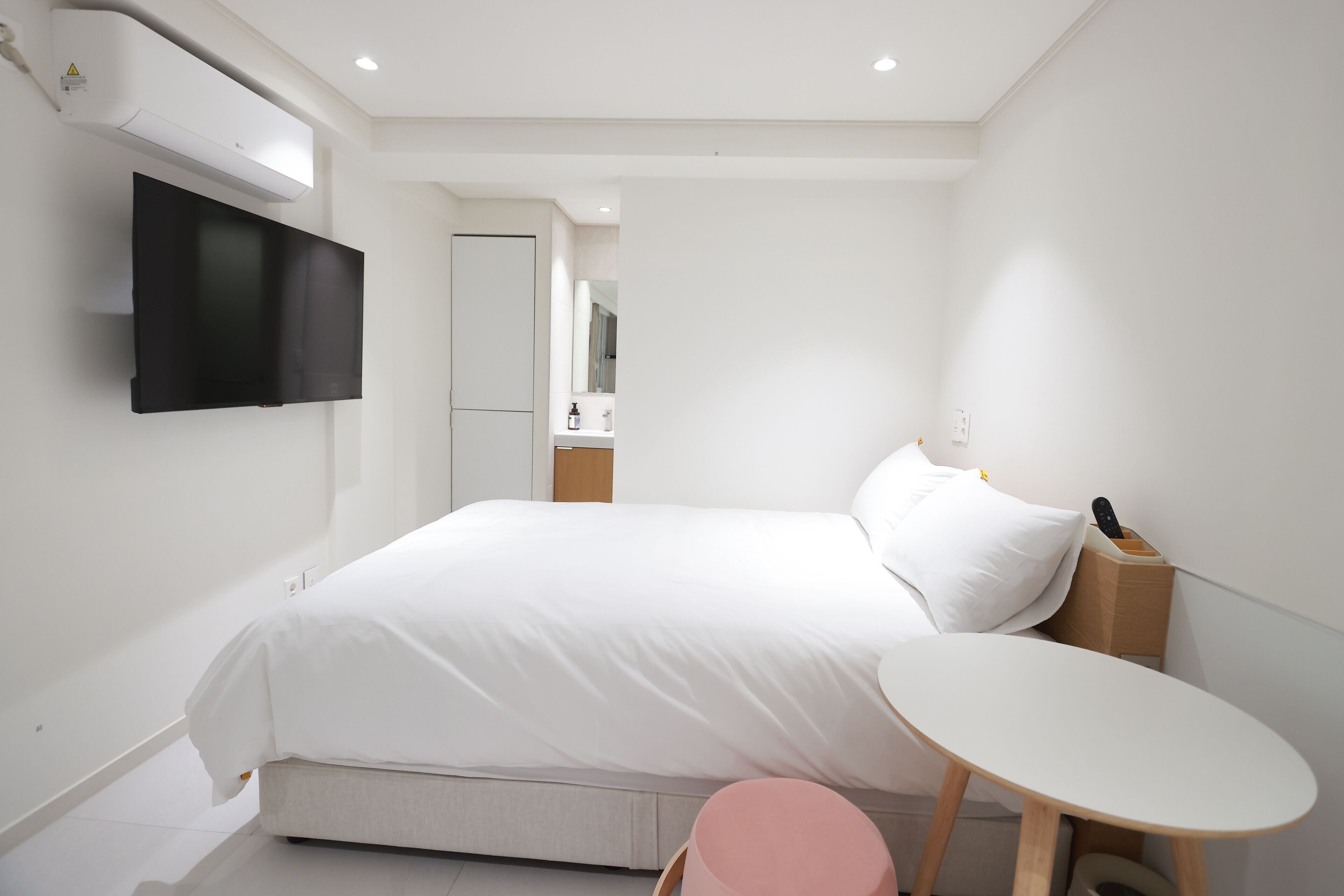 A modern hotel room with a bed, a small round table, a television mounted on the wall, and a mirror.